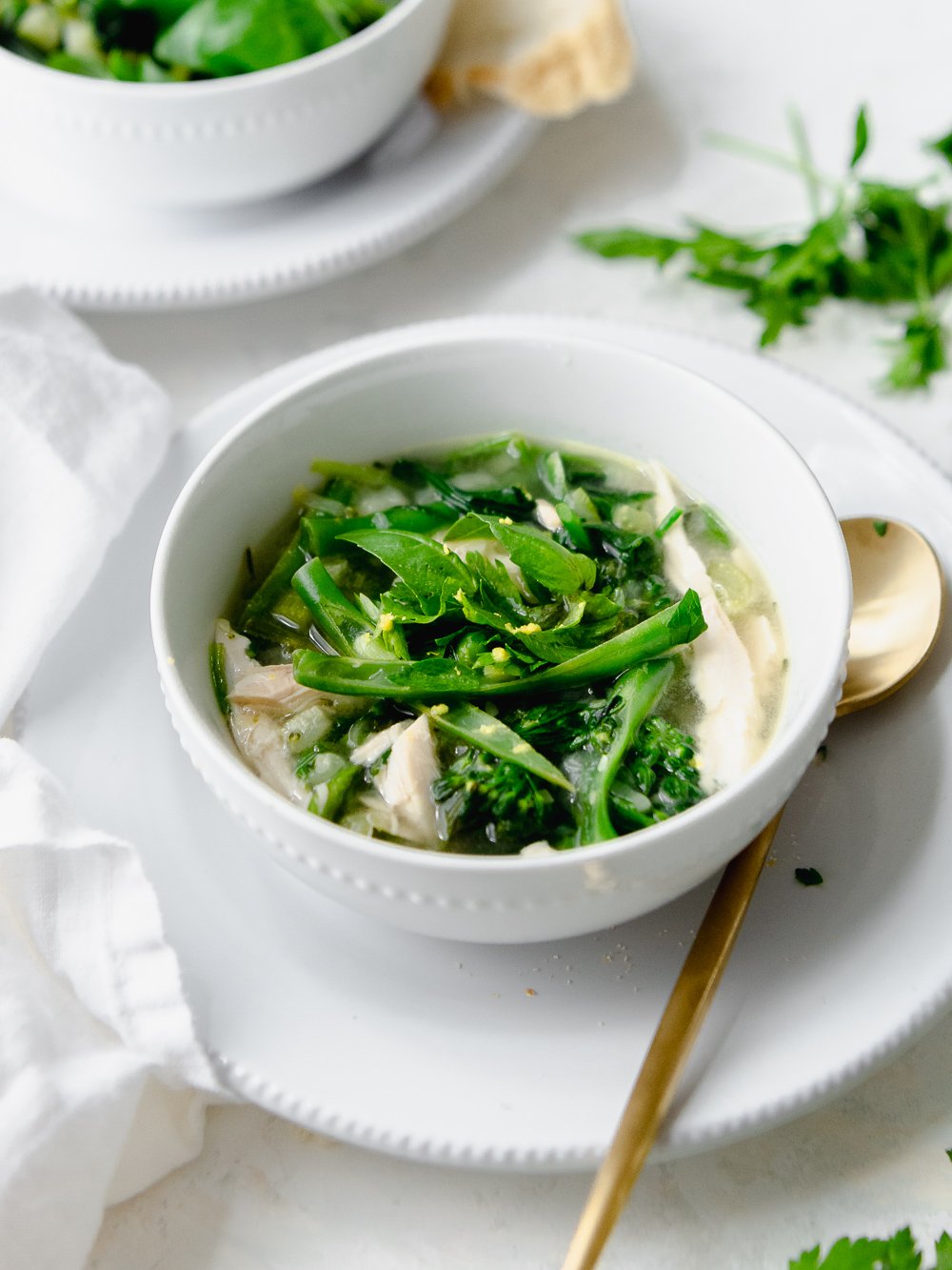 A close up of green minestrone soup with chicken garnished with basil and lemon zest, sitting on top of a plate with a gold spoon.