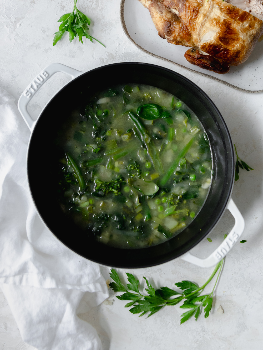 A white cast iron post with green minestrone soup next to a rotisserie chicken.