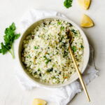 cauliflower rice pilaf in a medium grey serving bowl with lemon slides and parsley garnish to the side.