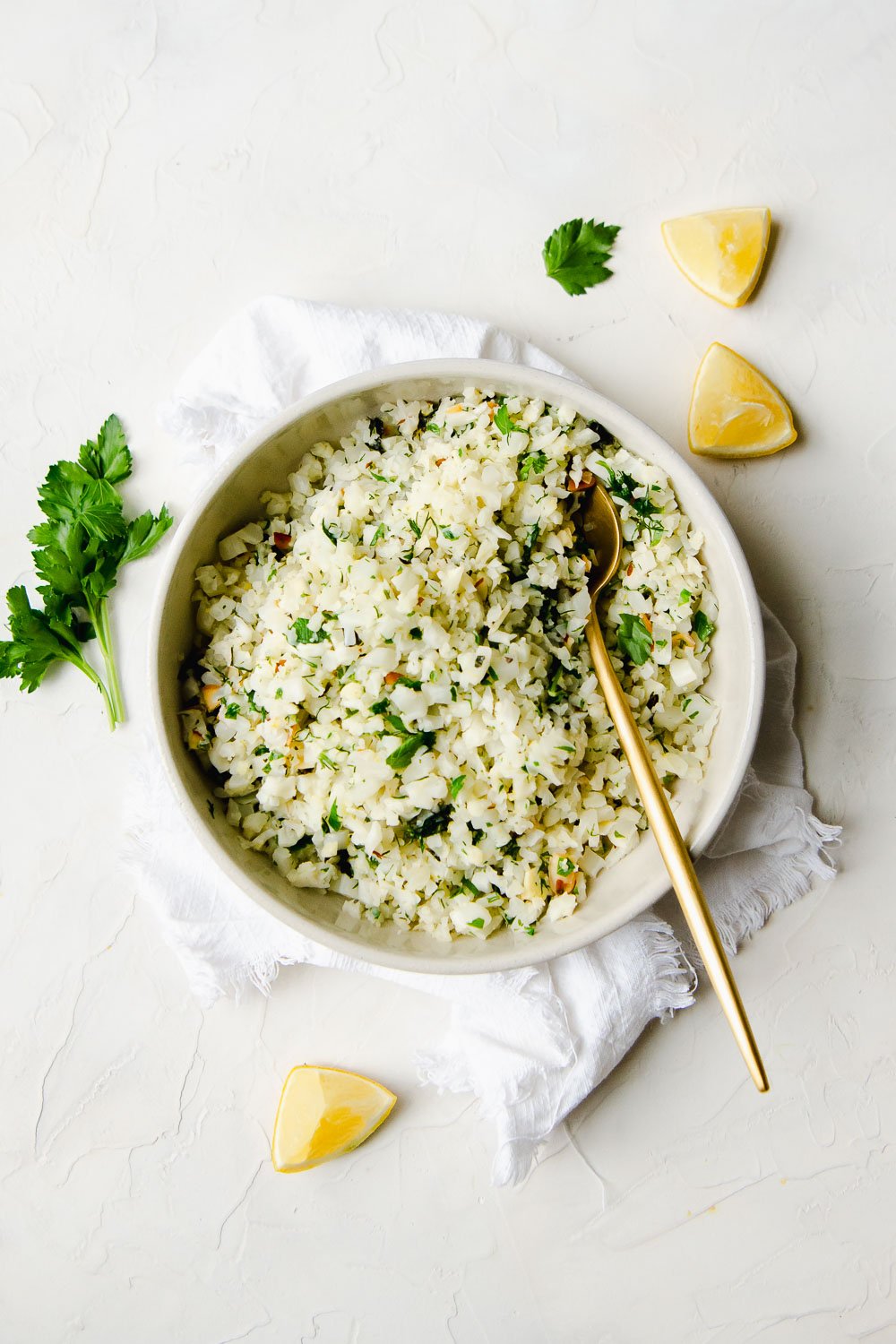 cauliflower rice pilaf in a medium grey serving bowl with lemon slides and parsley garnish to the side.