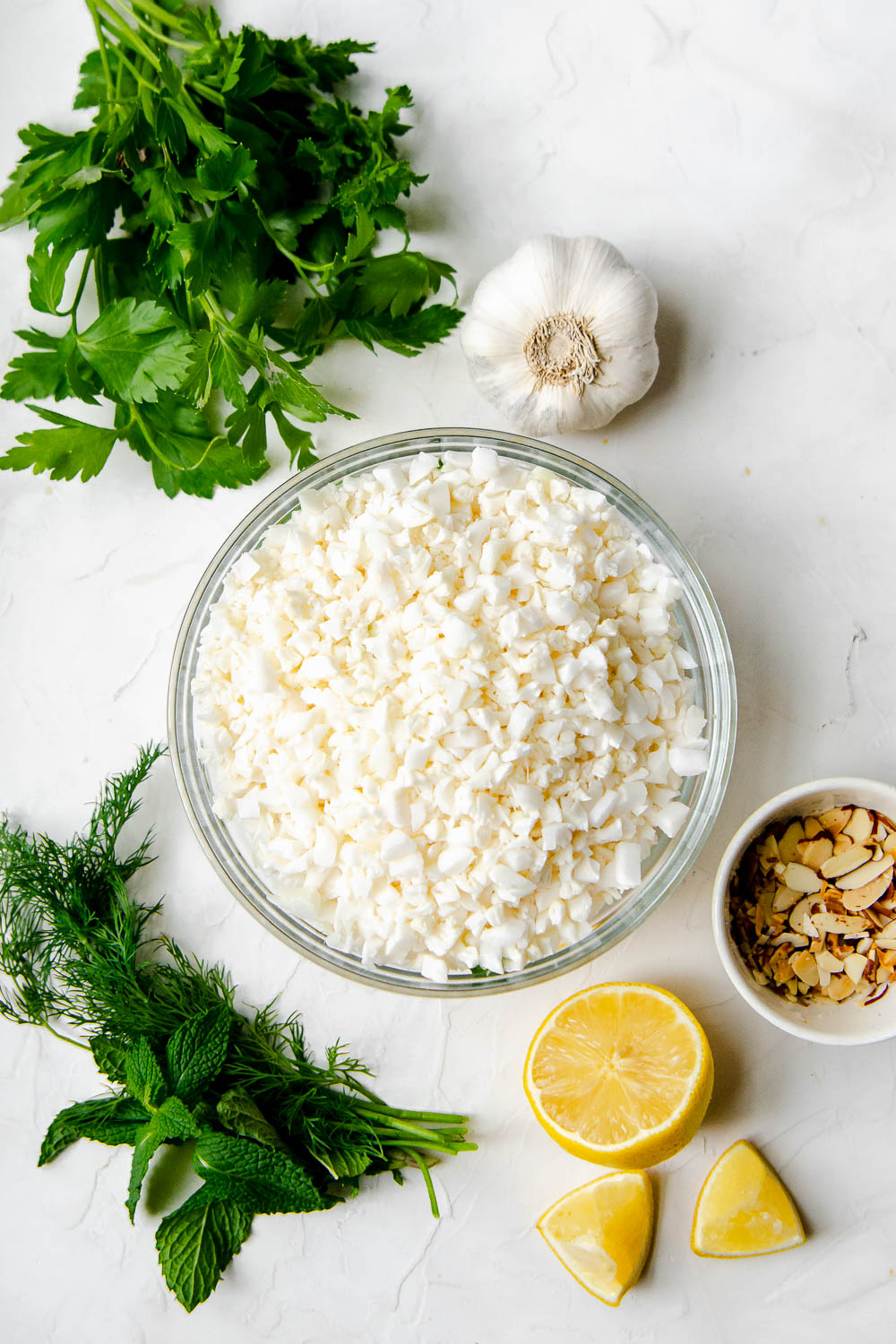 Ingredients for herbed cauliflower rice pilaf including lemons, dills, mint, parsley and toasted almonds.