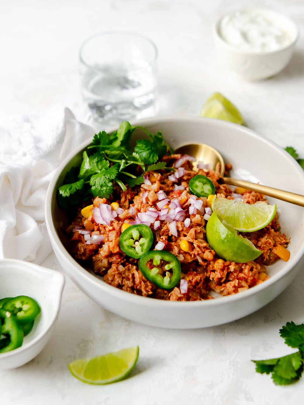 Close up of the one pot Mexican Chicken and Cauliflower Rice recipe garnished with red onions, jalapeños, limes and cilantro.