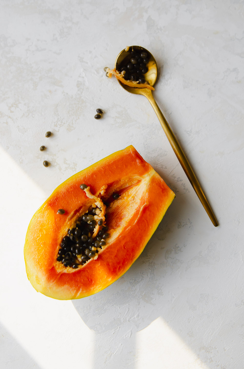 Close-up of half a papaya with seeds placed next to a gold spoon with sun coming in through the window.