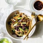 Egg roll in a bowl served with a green onions and a spicy chili tamari sauce.