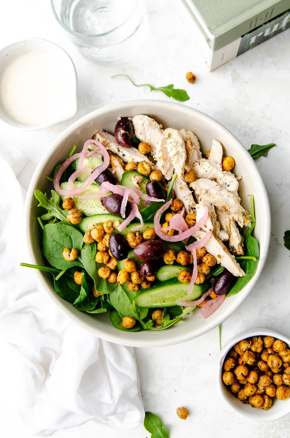 Bowl of arugula and spinach greens layered with kalamata olives, cucumbers, roasted chickpeas, greek grilled chicken and pickled onions. Served on the side with extra chickpeas and a bowl of tahini lemon dressing.